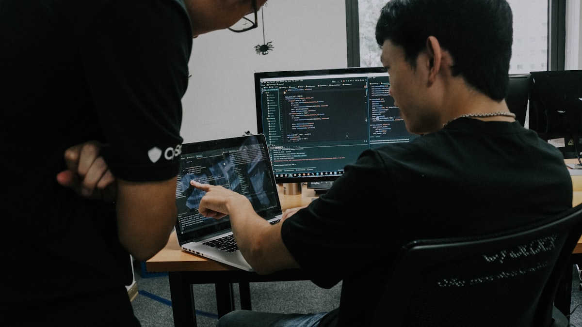 Two developers working side by side at their computers in an office, reviewing code together
