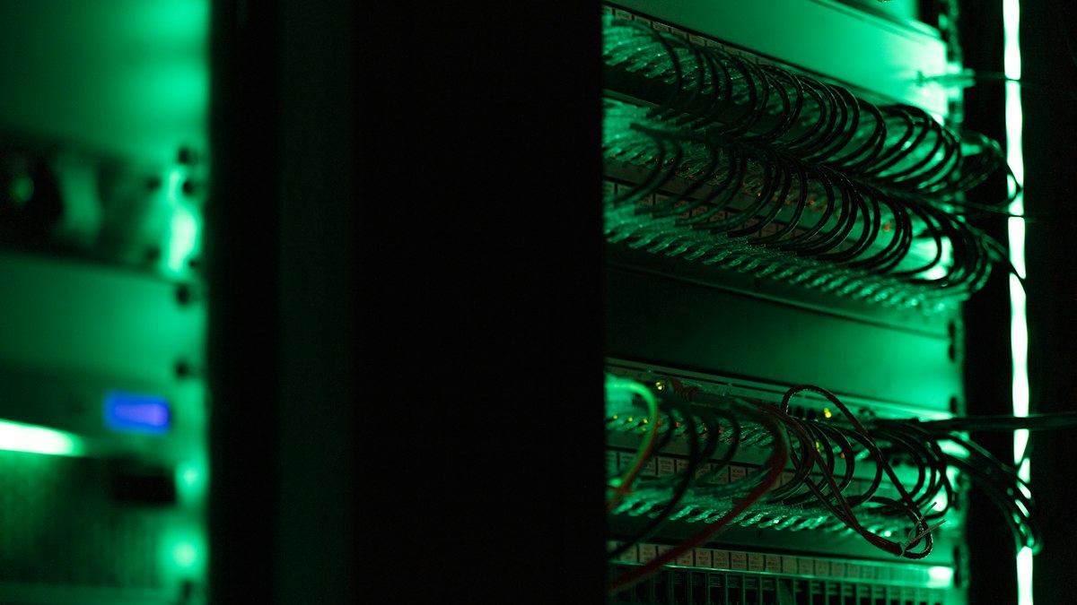 Server rack with patch-panel network cables lit in green inside a dark data center
